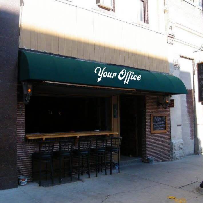 A storefront with a dark green awning that reads "Your Office" in white script font. Below the awning is a window-side bar with several black chairs lined up on the sidewalk. The building features brick and tan paneling with a chalkboard sign displayed near the entrance.