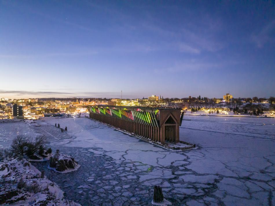 Marquette’s ore dock lit up with a holiday laser show on the frozen Lake Superior with the city lit up in the background.