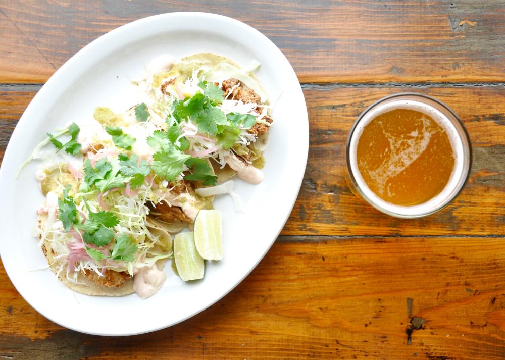 A pint of beer and a plate of fish tacos topped with fresh cilantro and lime wedges at Mongers Market and Kitchen