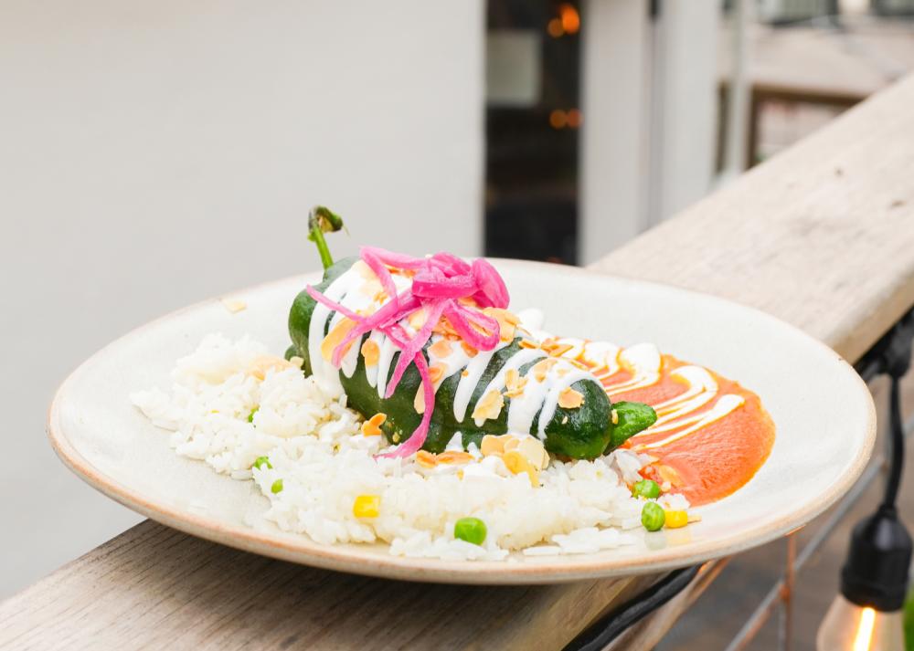 A plate with a poblano pepper dish on it sitting on a wooden railing outside of El Alma.