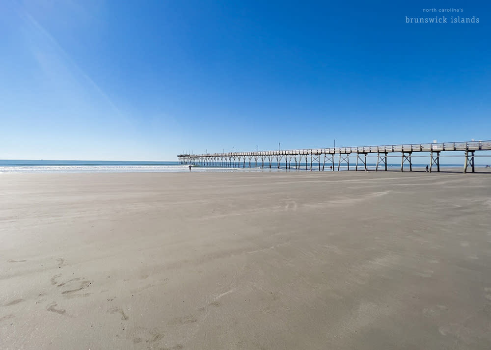 wide open beach with a pier in the background