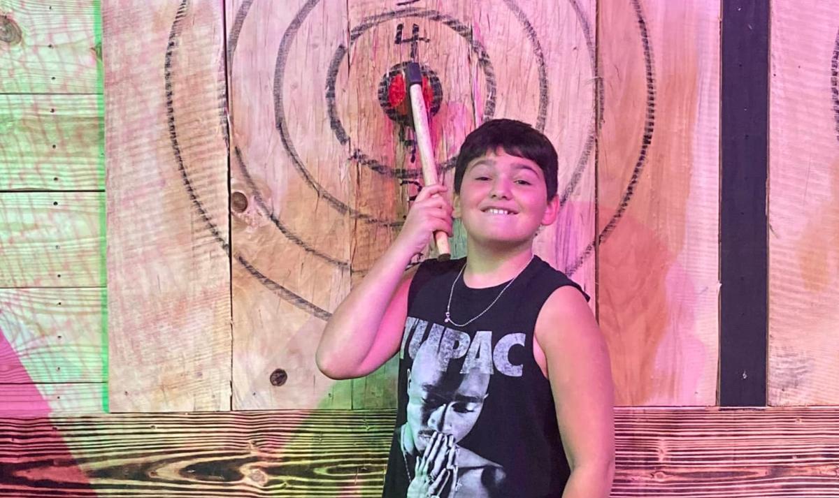 A young boy takes a photo near an axe thrown into a target at Kiss My Axe! Throwing