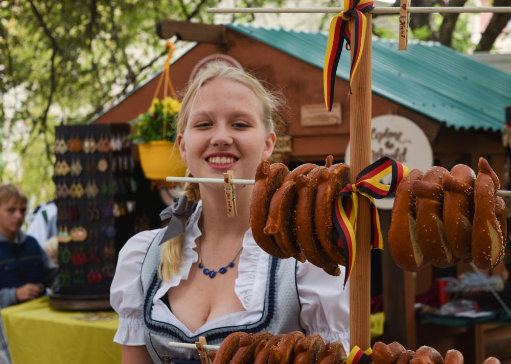 Woman in German clothing next to a stand of soft pretzels.