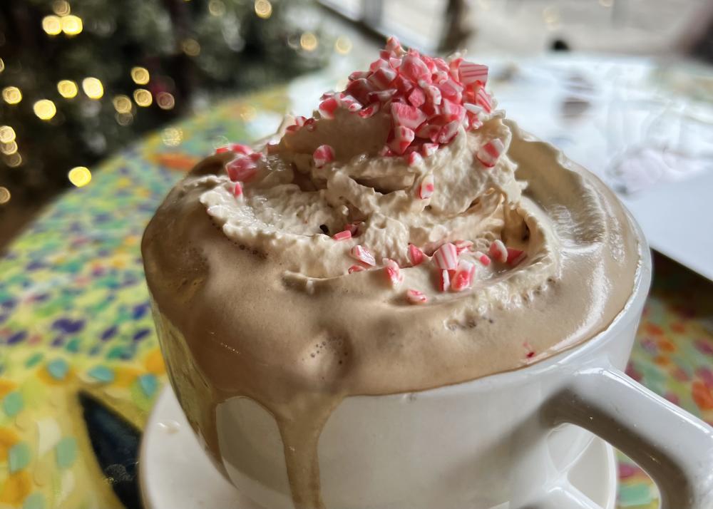a coffee mug filled with a latte and topped with whip cream and pieces of peppermint candy cane