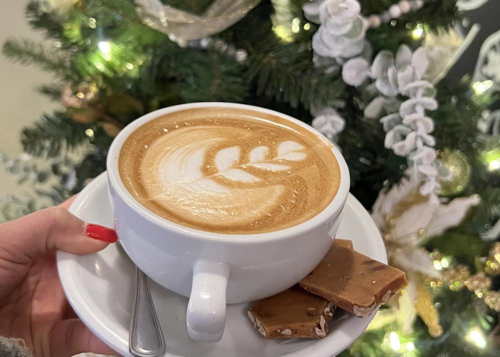 white mug with a latte and foam art in front of a christmas tree