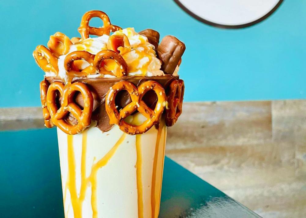 a milkshake with caramel pretzels candy bars and whipped cream on top
