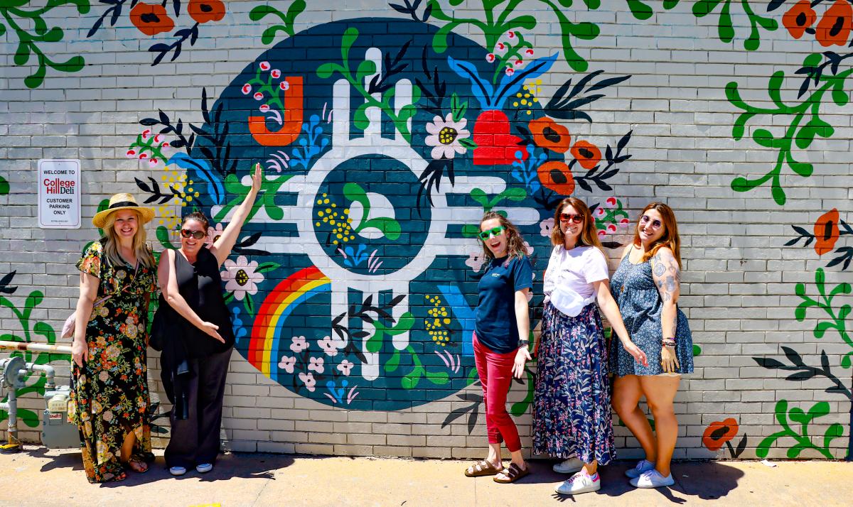 Women pose next to a mural in Wichita