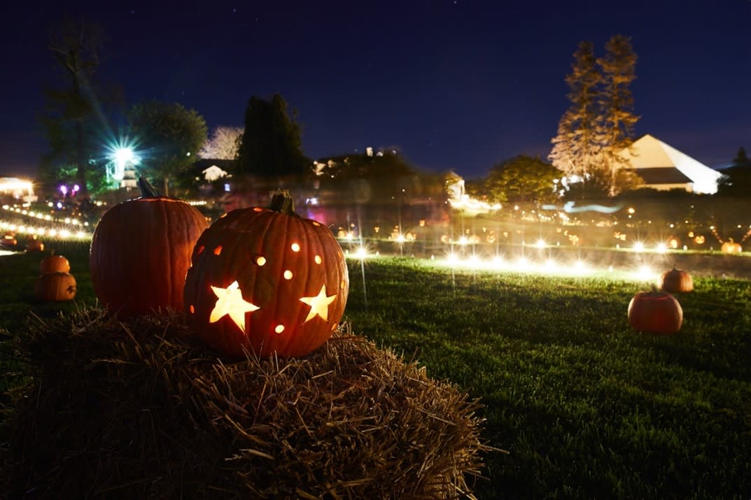 Illuminated pumpkin with star carving sitting on a hay bale