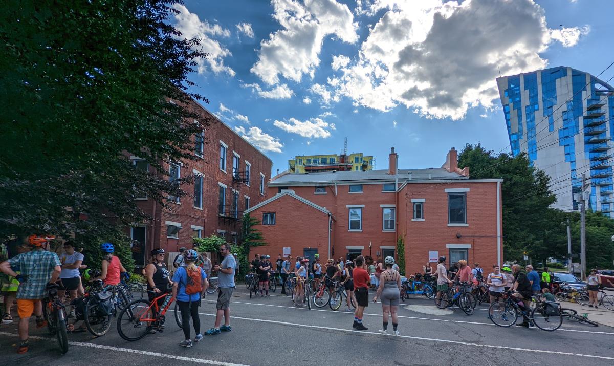 Lil's Bagels and the Ascent in the background with a crowd of bicycle riders standing