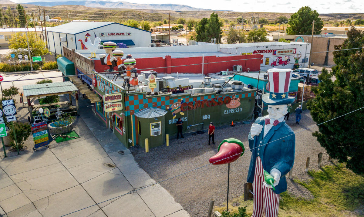 An aerial view of a colorful restaurant, adorned with many different cartoon characters statues, a hatch chile statue, and a large one of Uncle Sam in American regalia.