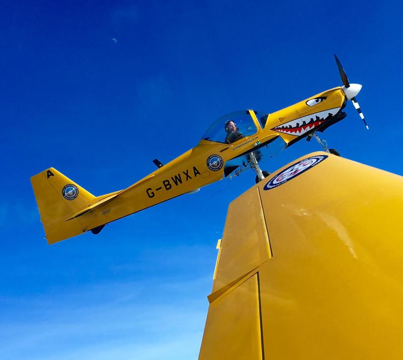 a yellow stunt aeroplane in the sky with a face painted on the nose