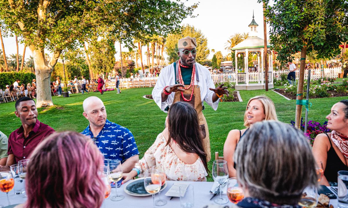 A server speaks to a group of festivalgoers at a table during Outstanding in the Field at Coachella 2023.