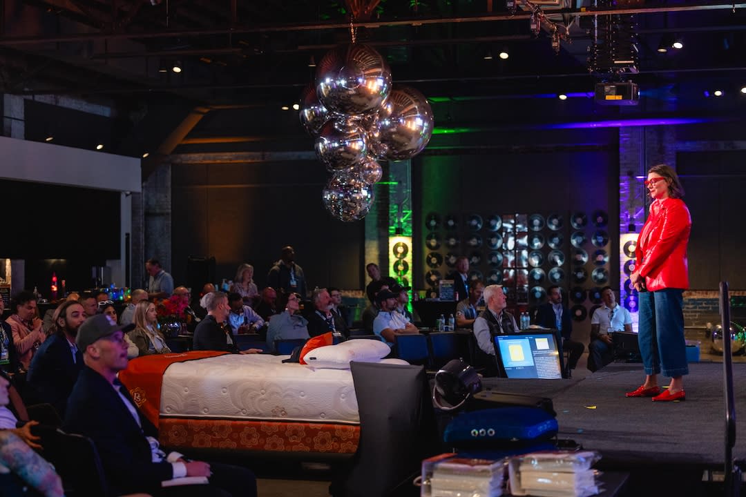 A speaker in a red jacket addresses Sleep Summit attendees at The Record in Bentonville, surrounded by disco balls and vinyl record décor.