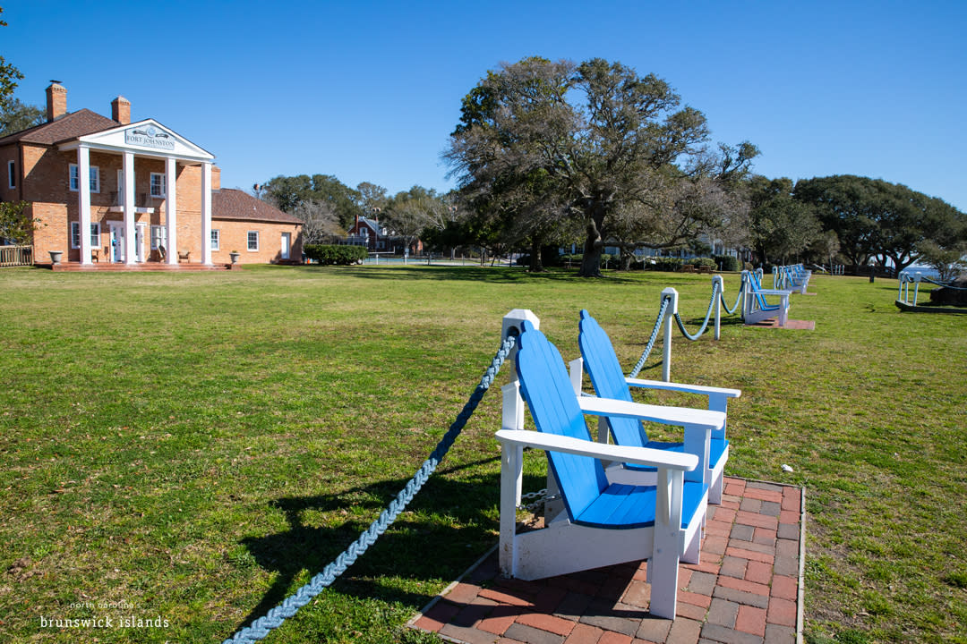 a brick building with blue deck chairs on a front lawn