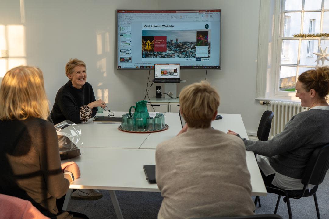 a group of people sat at a table having a meeting in front of a presentation screen
