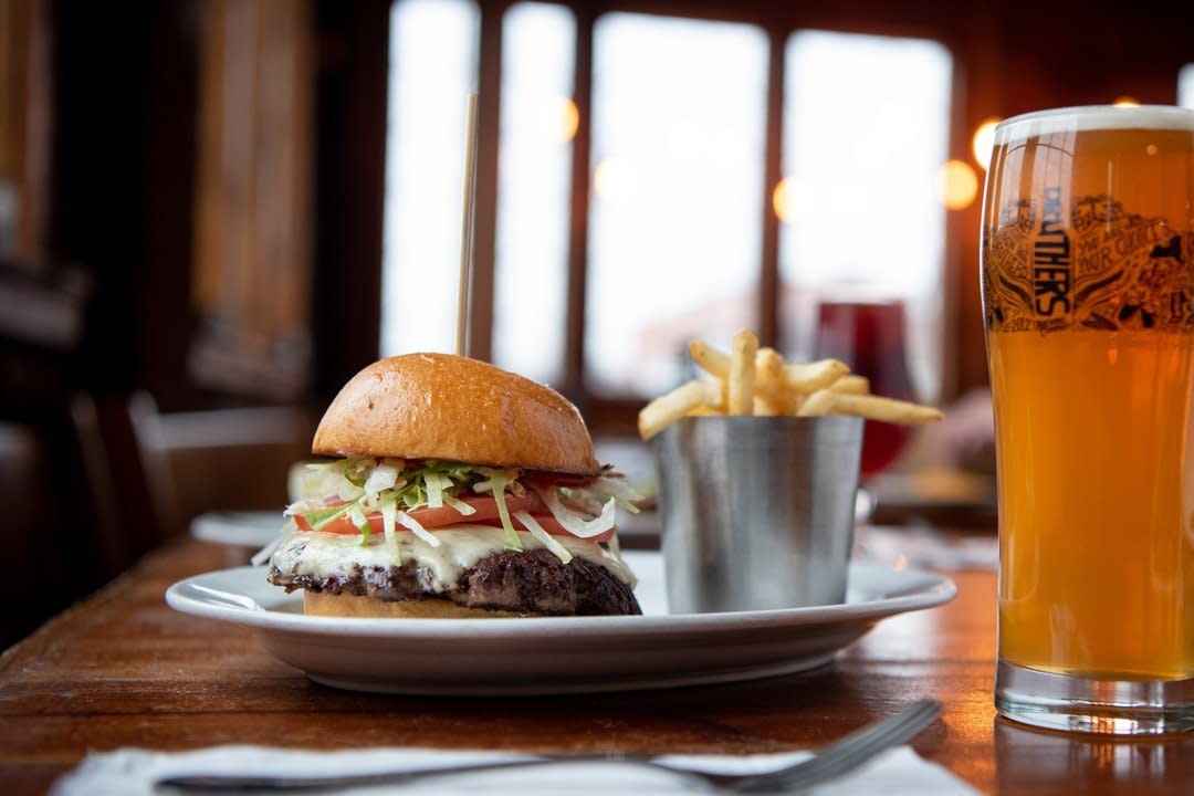 Plate with cheeseburger and fries, and a beer glass on a dining table