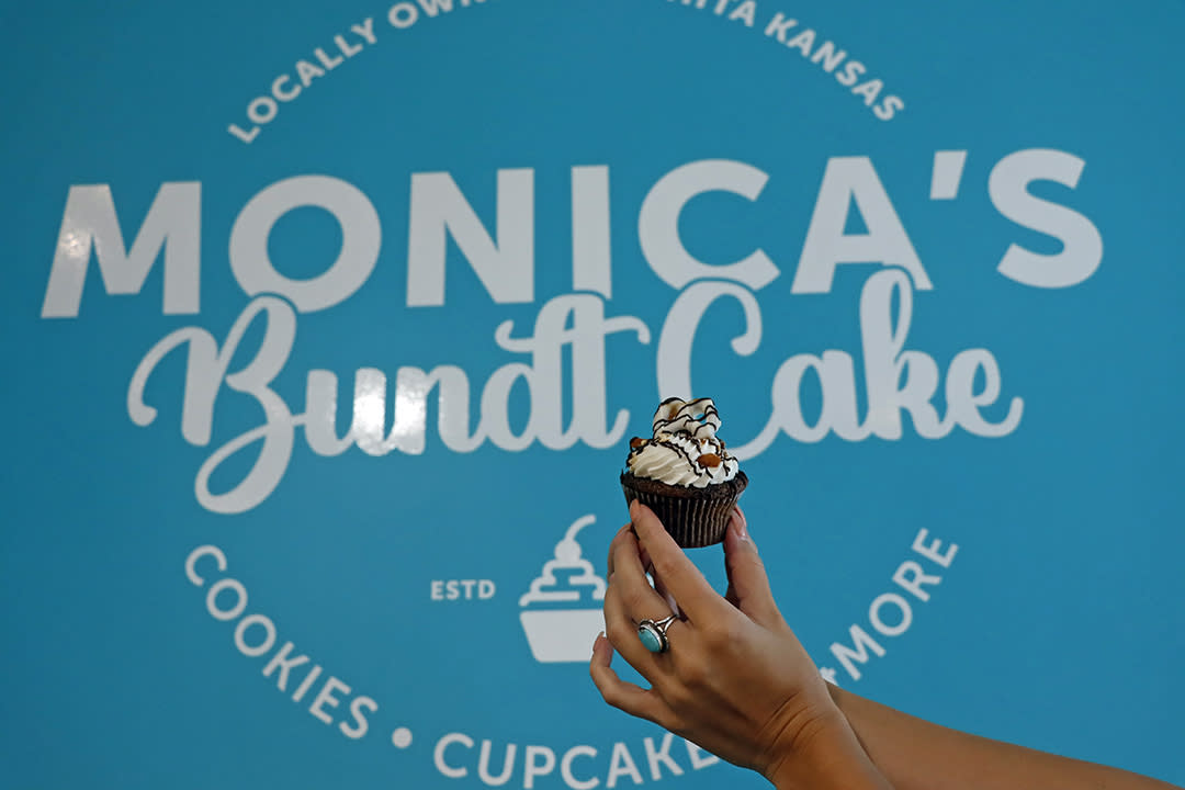 Miss Kansas holds a small cupcake up to the sign at Monica's Bundt Cake