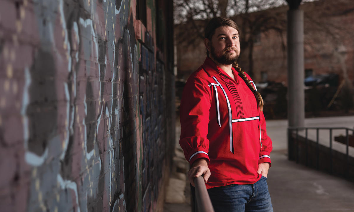 man in a red shirt standing by brick wall