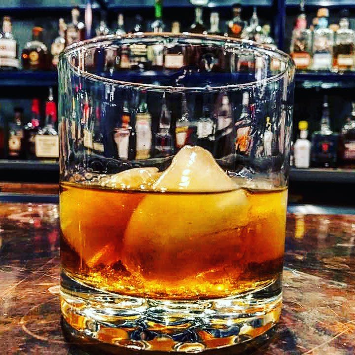 Closeup of bourbon cocktail in a clear glass with bourbon bottles in the background