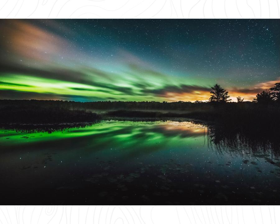 Green aurora and bright stars and constellation over inland lake in Marquette County, MI