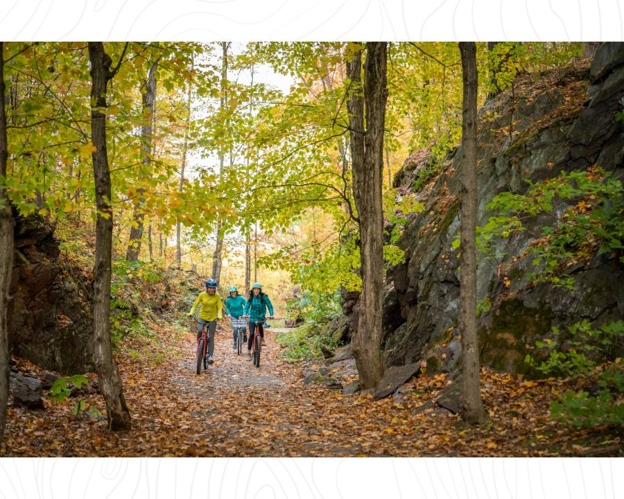 Three women biking on the paved IOHT surrounded by beautiful fall foliage and rock cuts