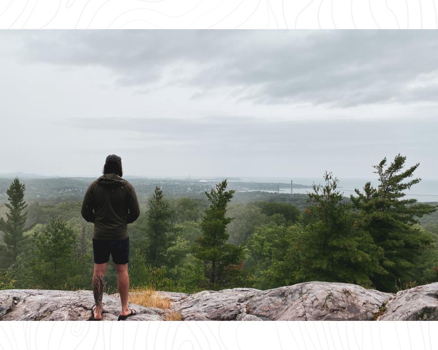 A hiker looking out over a foggy downtown Marquette and Lake Superior from the top of Mt. Marquette in the springtime