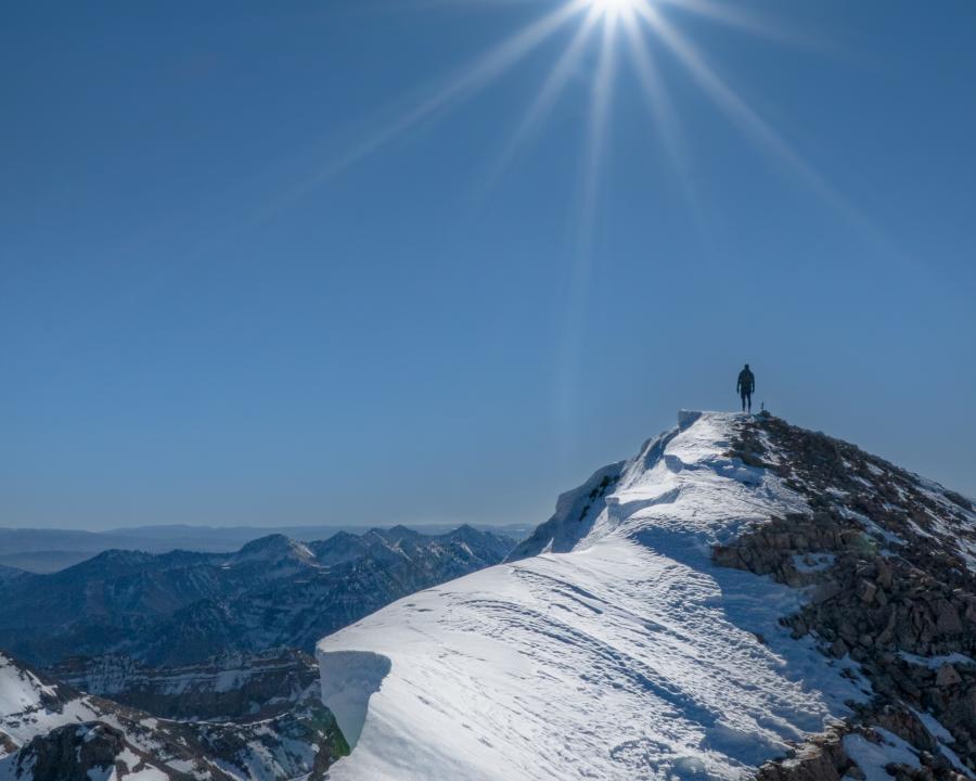 Man standing on peak of snowy mountain in the Utah Valley backcountry with sun shining