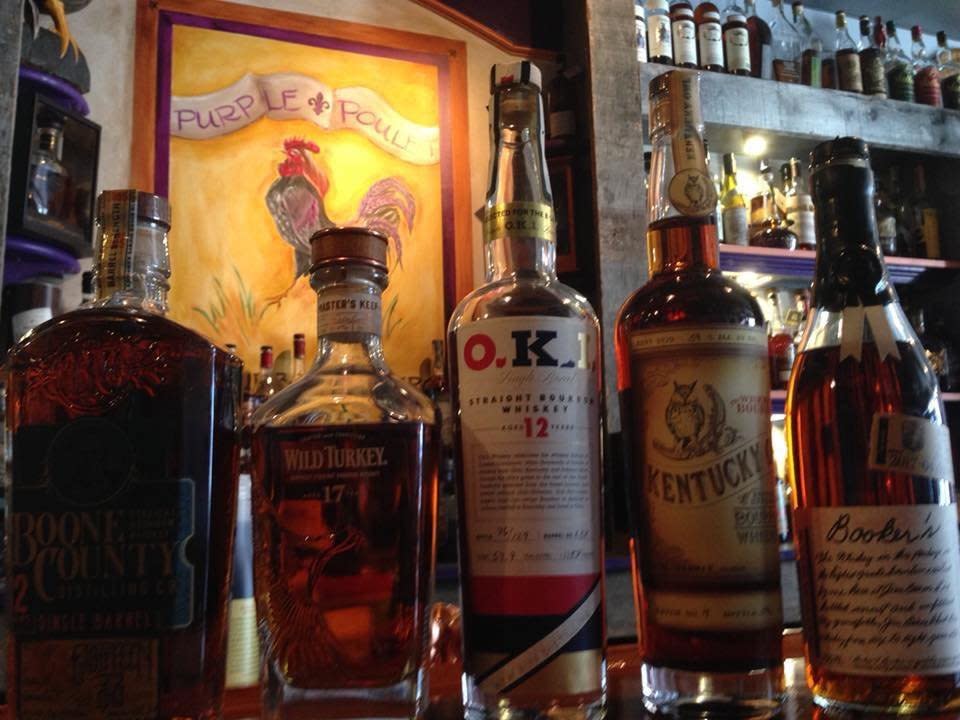 Sign for the Purple Poulet restaurant with a purple rooster behind a row of bourbon bottles