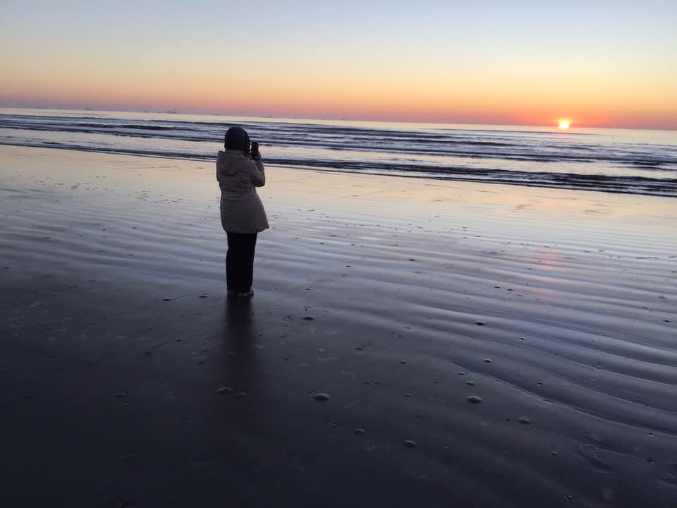 A silhouetted person stands on the beach at sunrise.