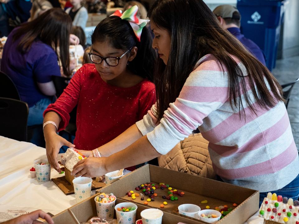 A woman helps a girl assemble a gingerbread house at Gingerbread Village at Exploration Place