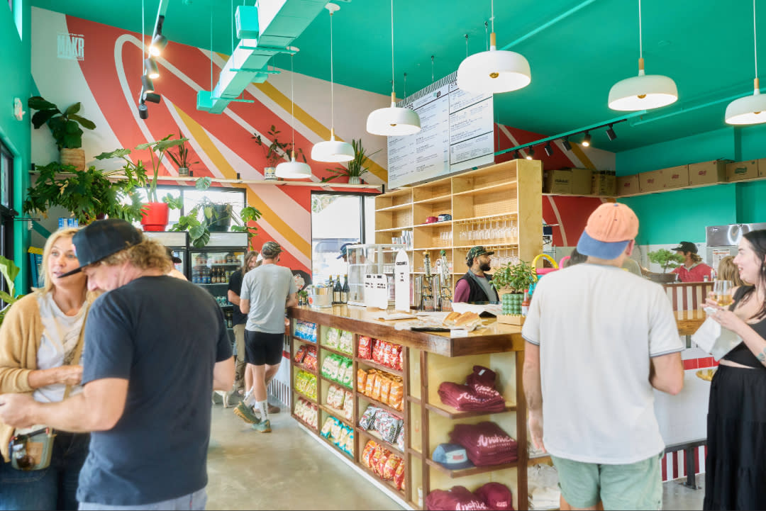 Interior of Archie’s Sandwichery in Bentonville, featuring a bright turquoise ceiling, colorful geometric wall mural, wooden counter service area, hanging lights, and customers gathering and ordering food inside the lively restaurant.