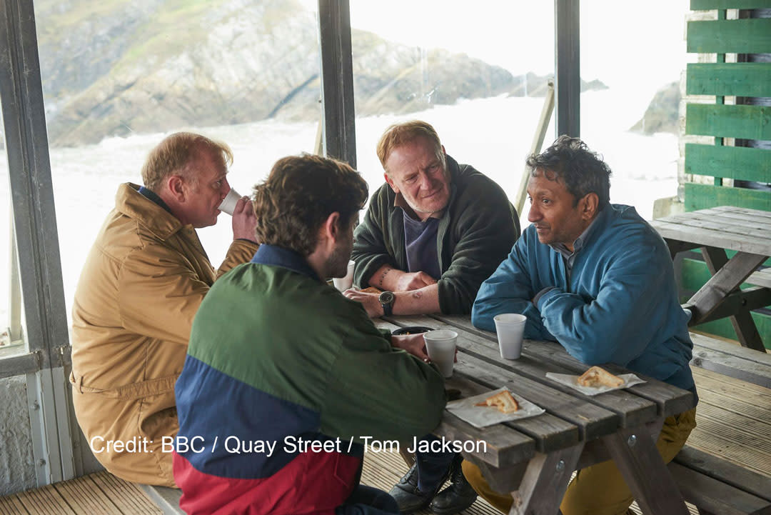 Four men sitting around a picnic bench.