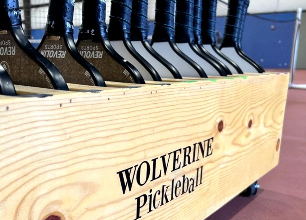 Pickelball paddles properly placed in a wooden paddle holder that is labeled "Wolverine Pickleball"