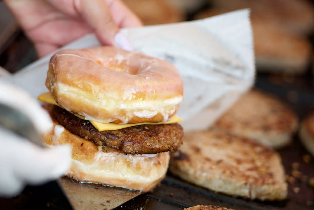 A hand picking up a sandwich made with a glazed donut, goetta, and cheese