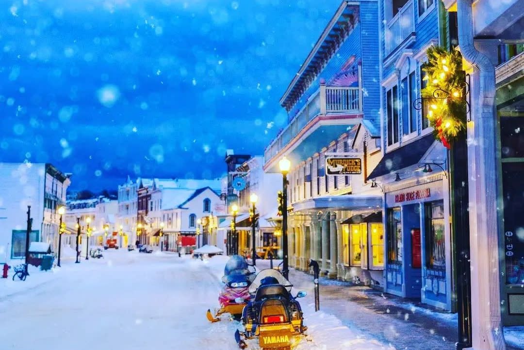 Snowmobiles line the side of Mackinac Island’s Main Street as snowflakes and darkness descend