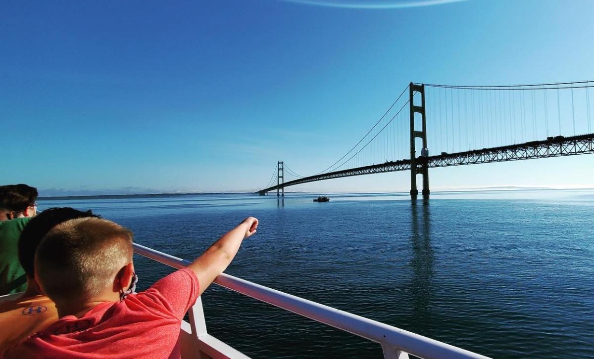 A boy on top deck of a Mackinac Island ferry boat points at the Mackinac Bridge