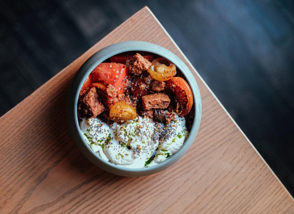 Bowl of seasoned vegetable, cubes of meat and a cream sauce topped with herb oil.