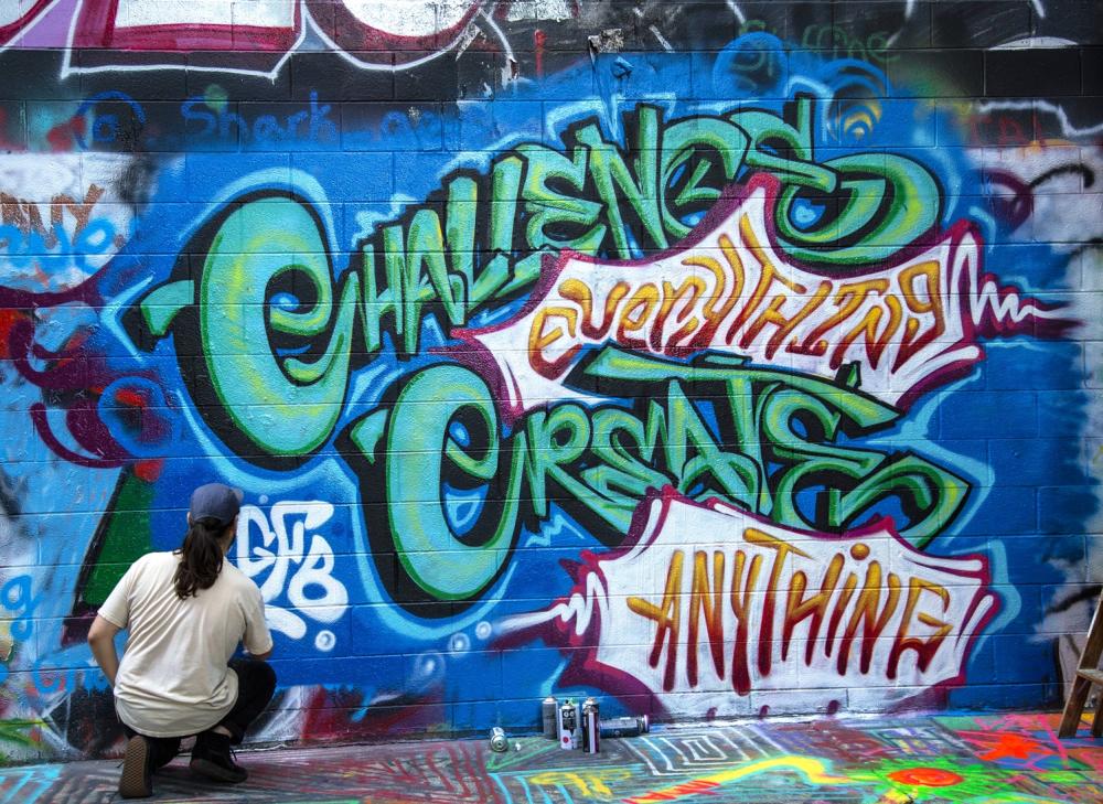 Person spraypainting "Challenge everything create anything mural in graffiti alley"