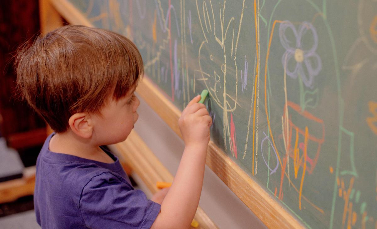 a small child draws on a busy chalkboard