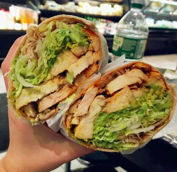 A lunch wrap is being held up filled with lettuce, chicken, avocado and more.