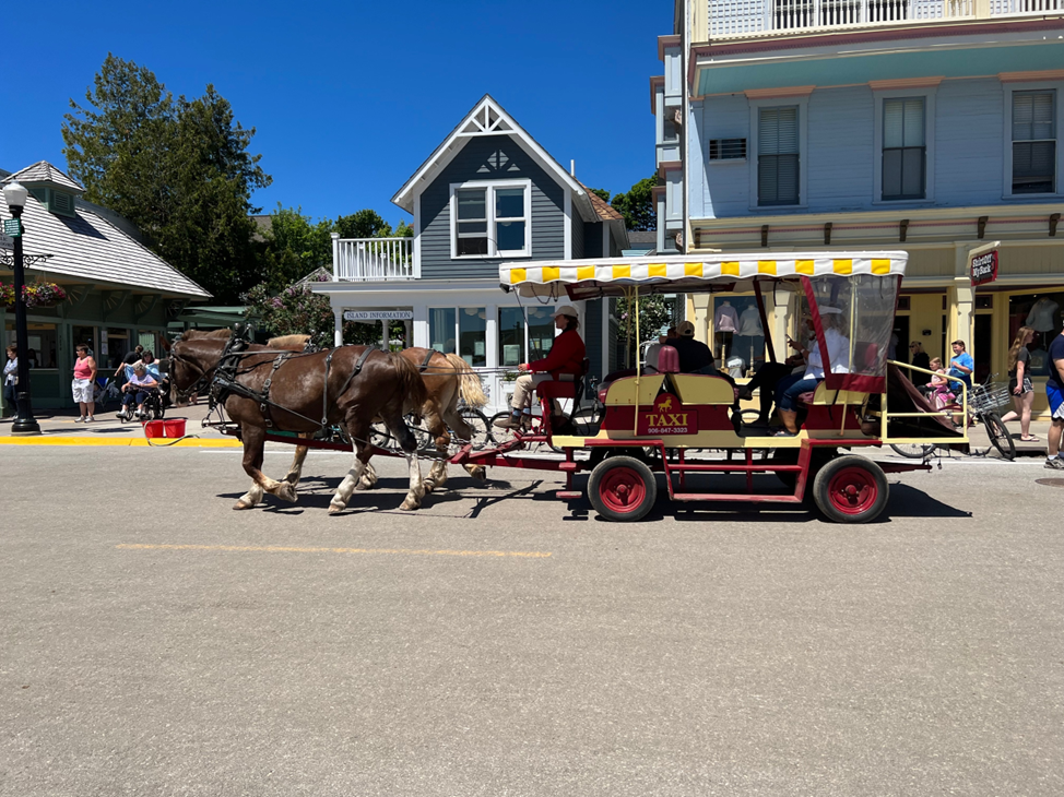 A horse-drawn taxi takes passengers down Mackinac Island’s Main Street on a sunny summer day.