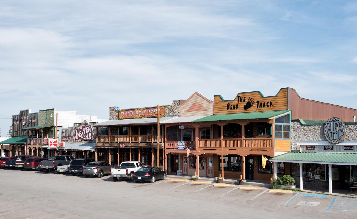 Row of old-Western style storefronts under a clear sky with parked cars in front.