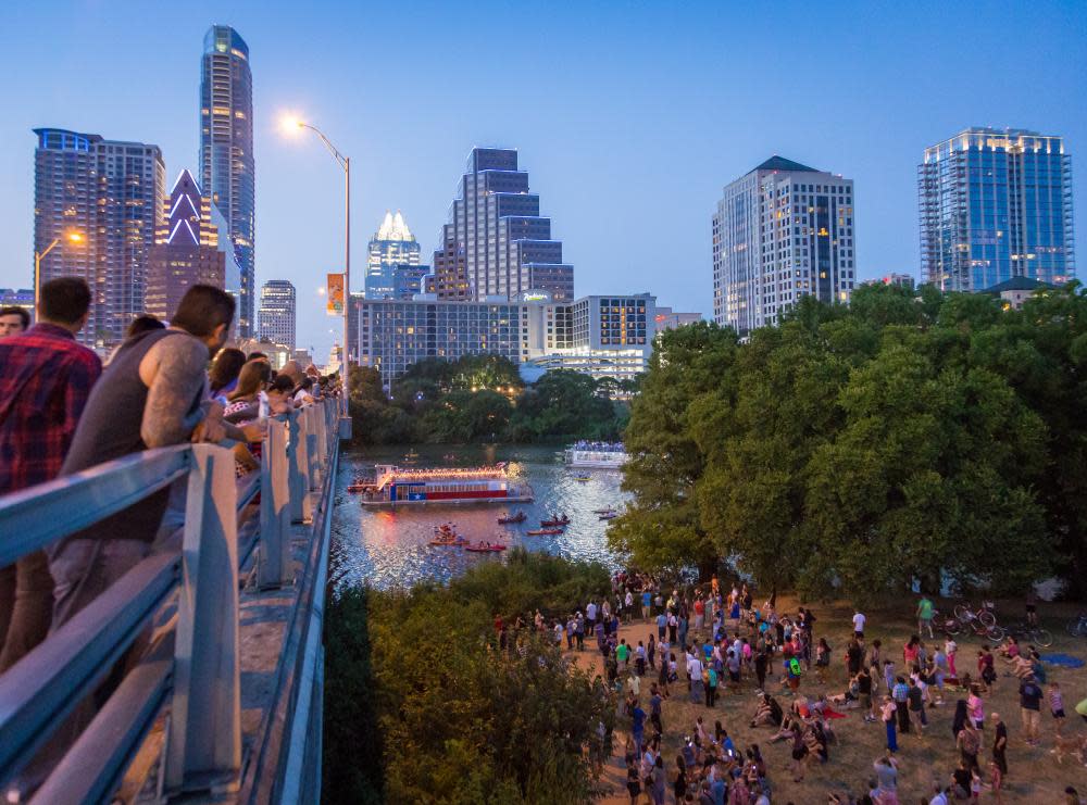 people standing on Congress Avenue bridge waiting for bats to emerge at dusk in front of downtown Austin skyline