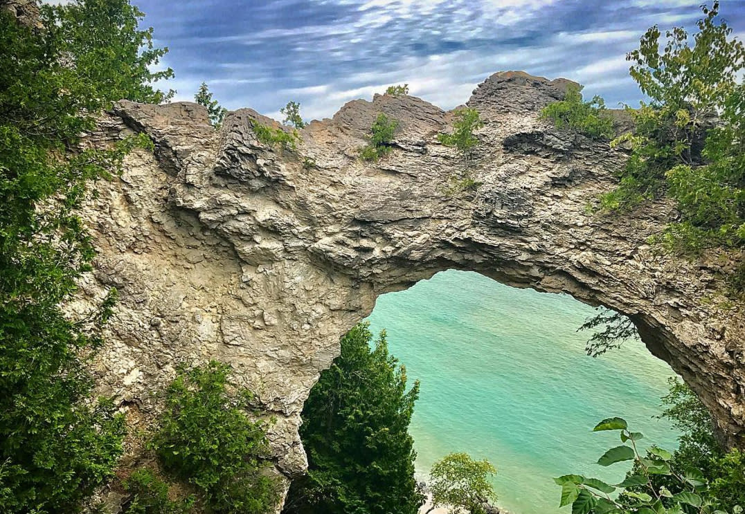 Mackinac Island’s Arch Rock with cloudy blue sky above and teal water of Lake Huron below