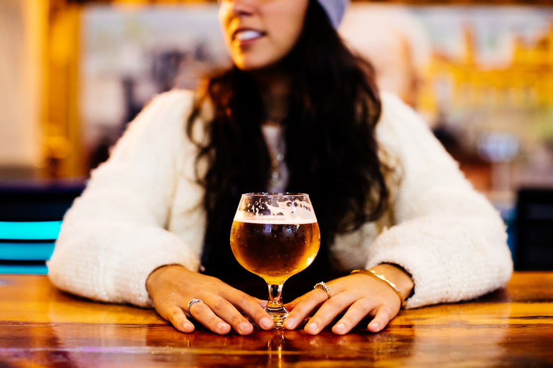 A woman sits at the bar with a beer in a goblet glass at Tarpon River Brewery.