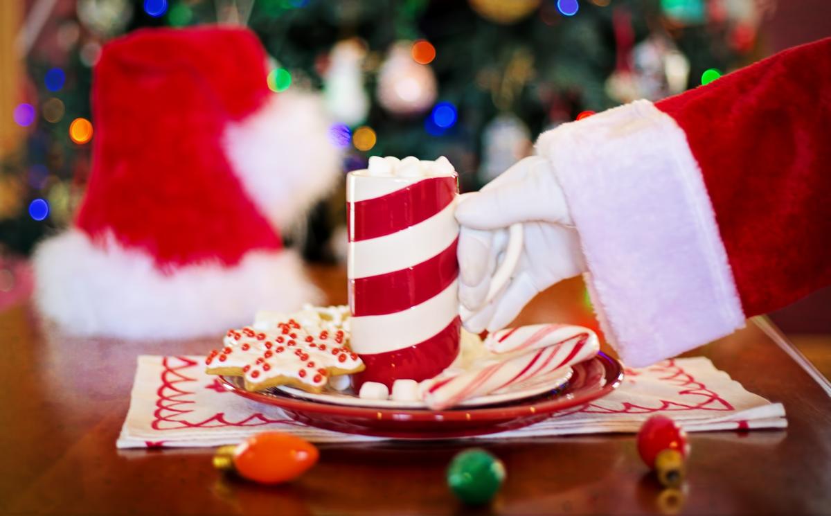 Santa touching cookies, hot cocoa, and a candy cane.