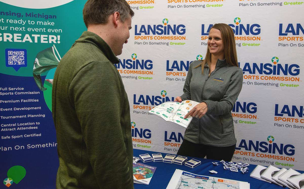 A Lansing Sports Commission staff member shares visitor information at a welcome booth.