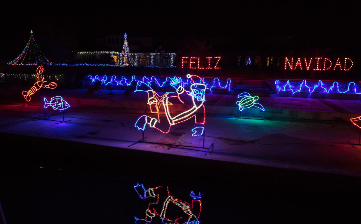 A festive display featuring brightly lit Christmas decorations, including an outline of Santa Claus and aquatic animals. The phrase 'Feliz Navidad' is illuminated in red lights.