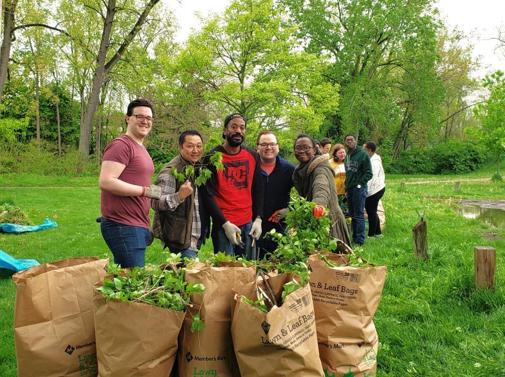 five people pose in front of filled lawn leave clean up bags during a park cleanup day.