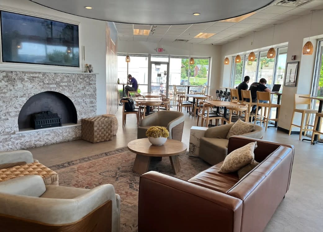 Interior of Qamari Yemeni Coffee in Milwaukee, featuring modern seating with armchairs and tables, a fireplace, and large windows letting in natural light.